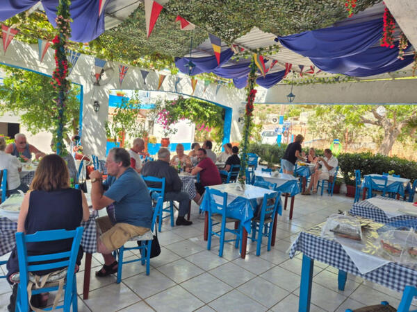 Outdoor terrace at Taverna Exanti with blue chairs, shaded tables and guests dining in Exanti, Crete.